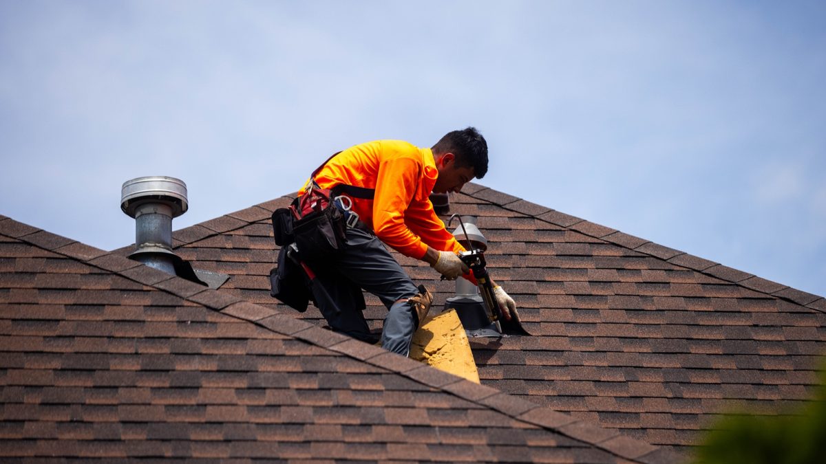 A roofer working on a shingled roof on a job site, hands full